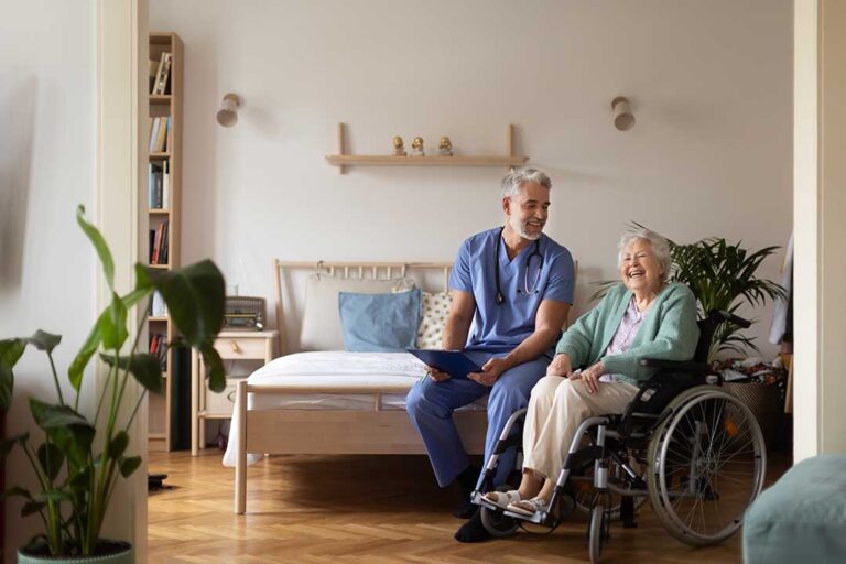 A senior sitting with a friend, sharing conversation and tea in a bright living room.